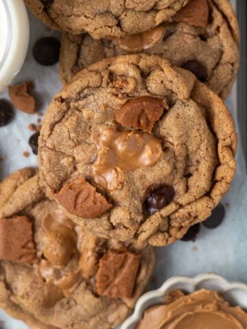 over head look at biscoff chocolate chip cookie on a parchment lined cookie sheet with a glass of milk and a bowl of cookie butter