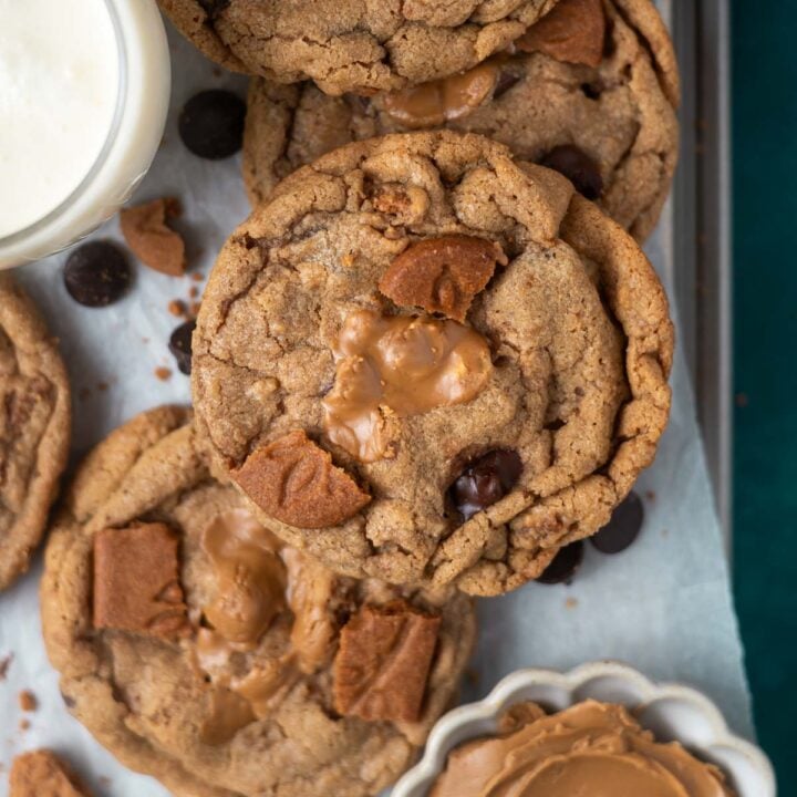 over head look at biscoff chocolate chip cookie on a parchment lined cookie sheet with a glass of milk and a bowl of cookie butter
