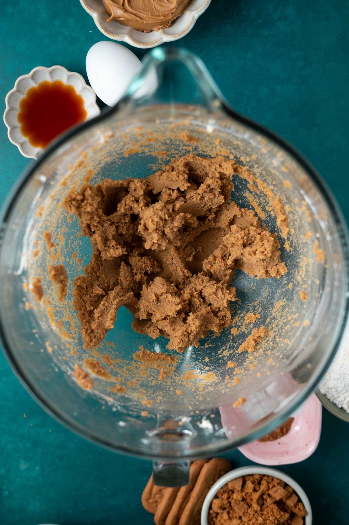 butter and sugars beaten together in a glass bowl with egg, vanilla, cookie butter and speculoos cookies on the counter
