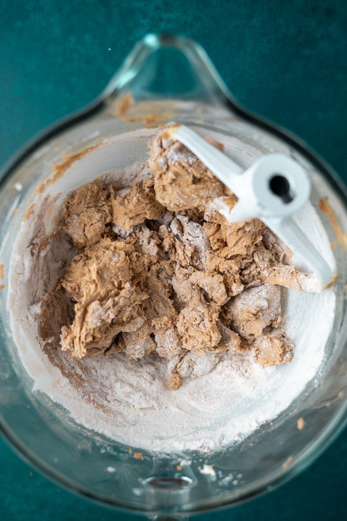cookie dough in a mixer bowl with large streaks of flour remaining