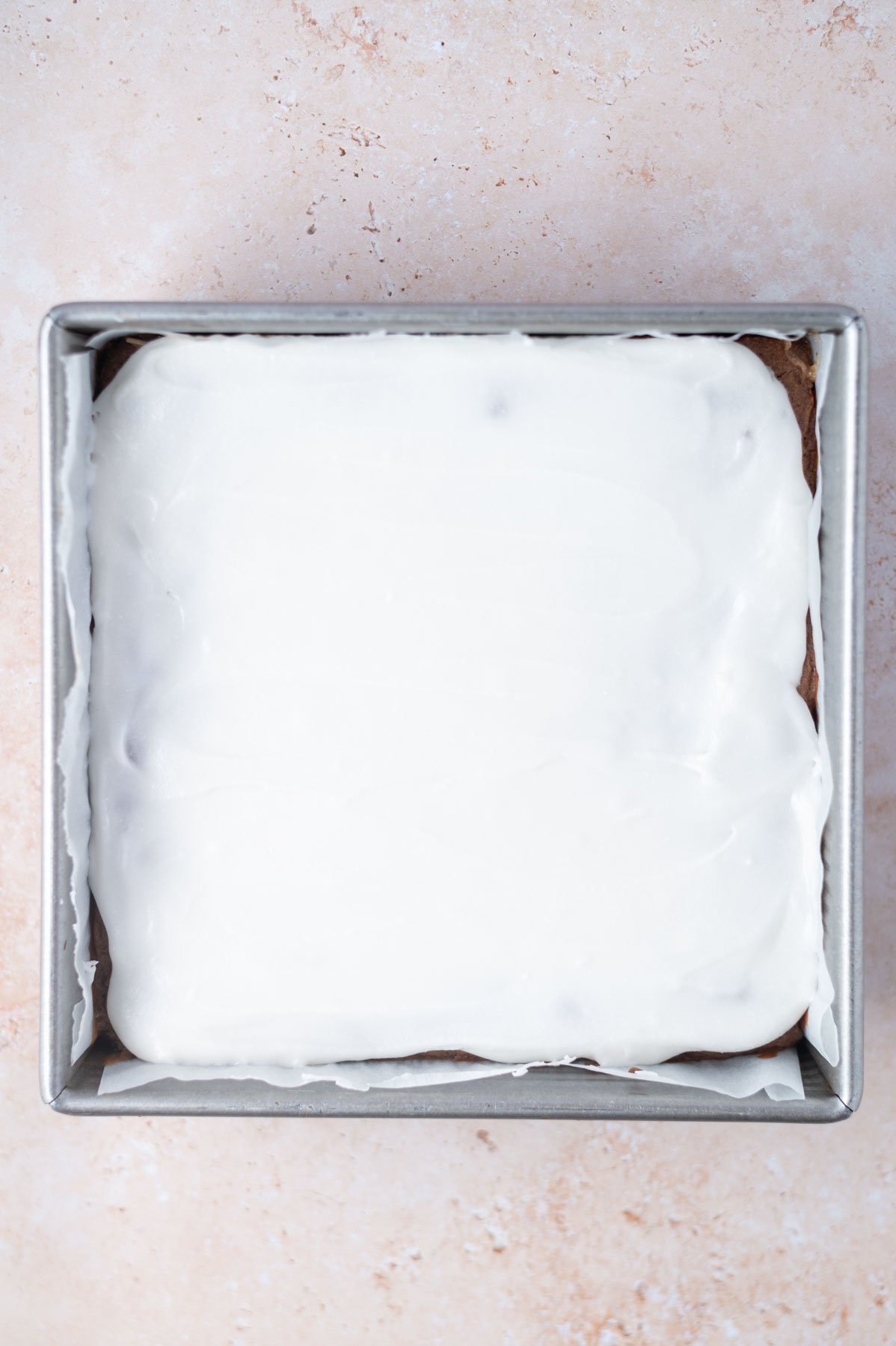 coconut glaze over top of brownies in a baking tin