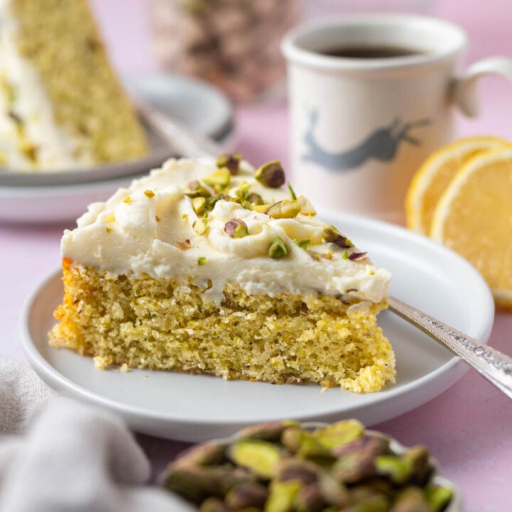 slice of lemon pistachio cake on a plate with a fork and a cup of coffee and lemon slices in the background
