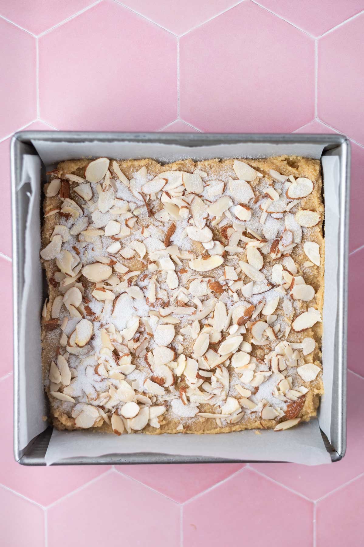 sliced almonds and sugar sprinkled over batter in a parchment lined baking pan