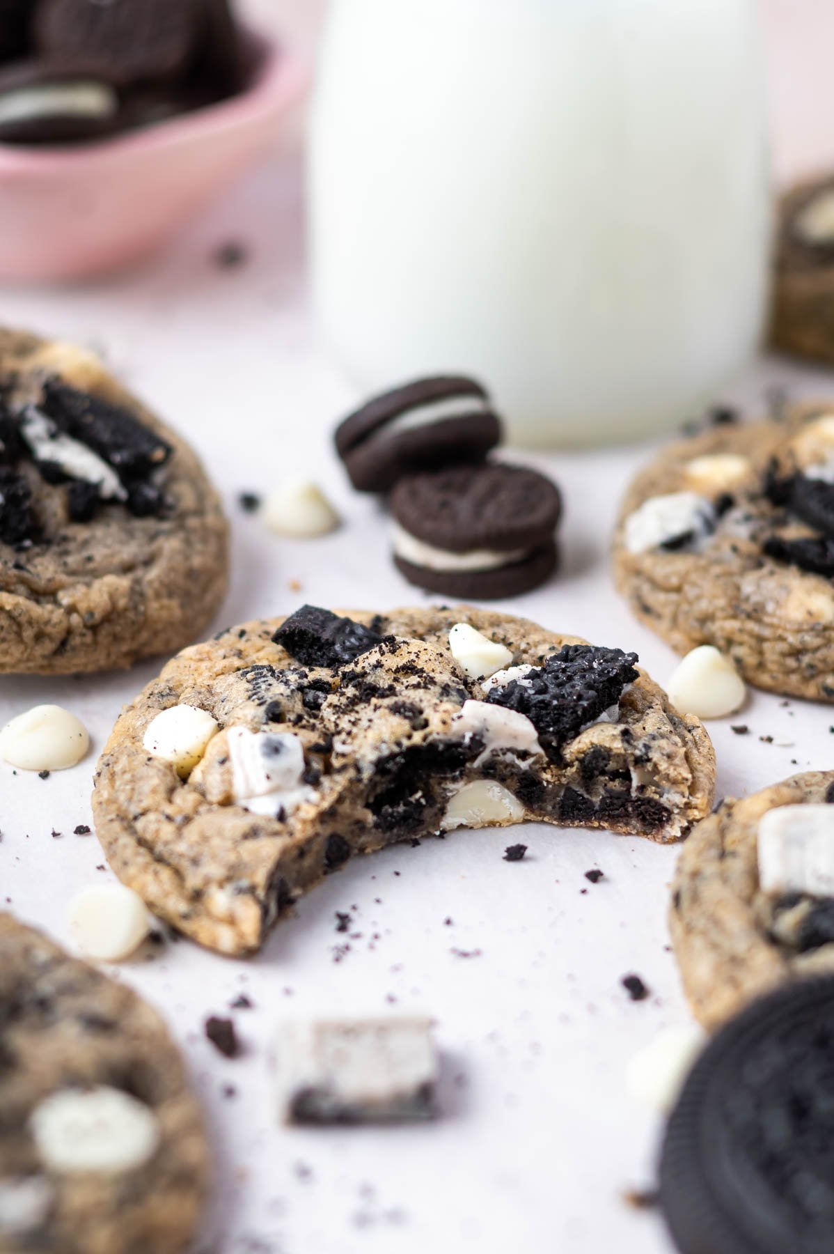 cookies n cream cookie with a bite missing on parchment paper with oreo cookie pieces and white chocolate chips