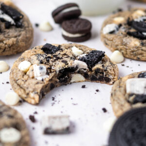 cookies n cream cookie with a bite missing on parchment paper with oreo cookie pieces and white chocolate chips