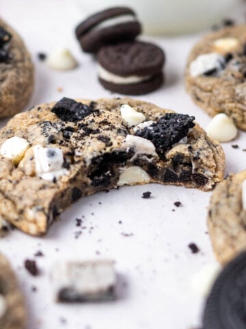 cookies n cream cookie with a bite missing on parchment paper with oreo cookie pieces and white chocolate chips