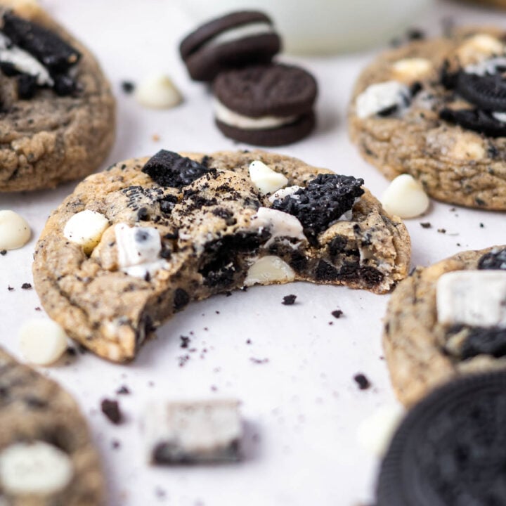 cookies n cream cookie with a bite missing on parchment paper with oreo cookie pieces and white chocolate chips