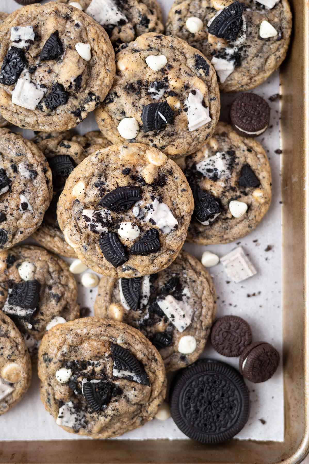 pile of cookies on a parchment lined baking sheet with extra oreo cookies and white chocolate