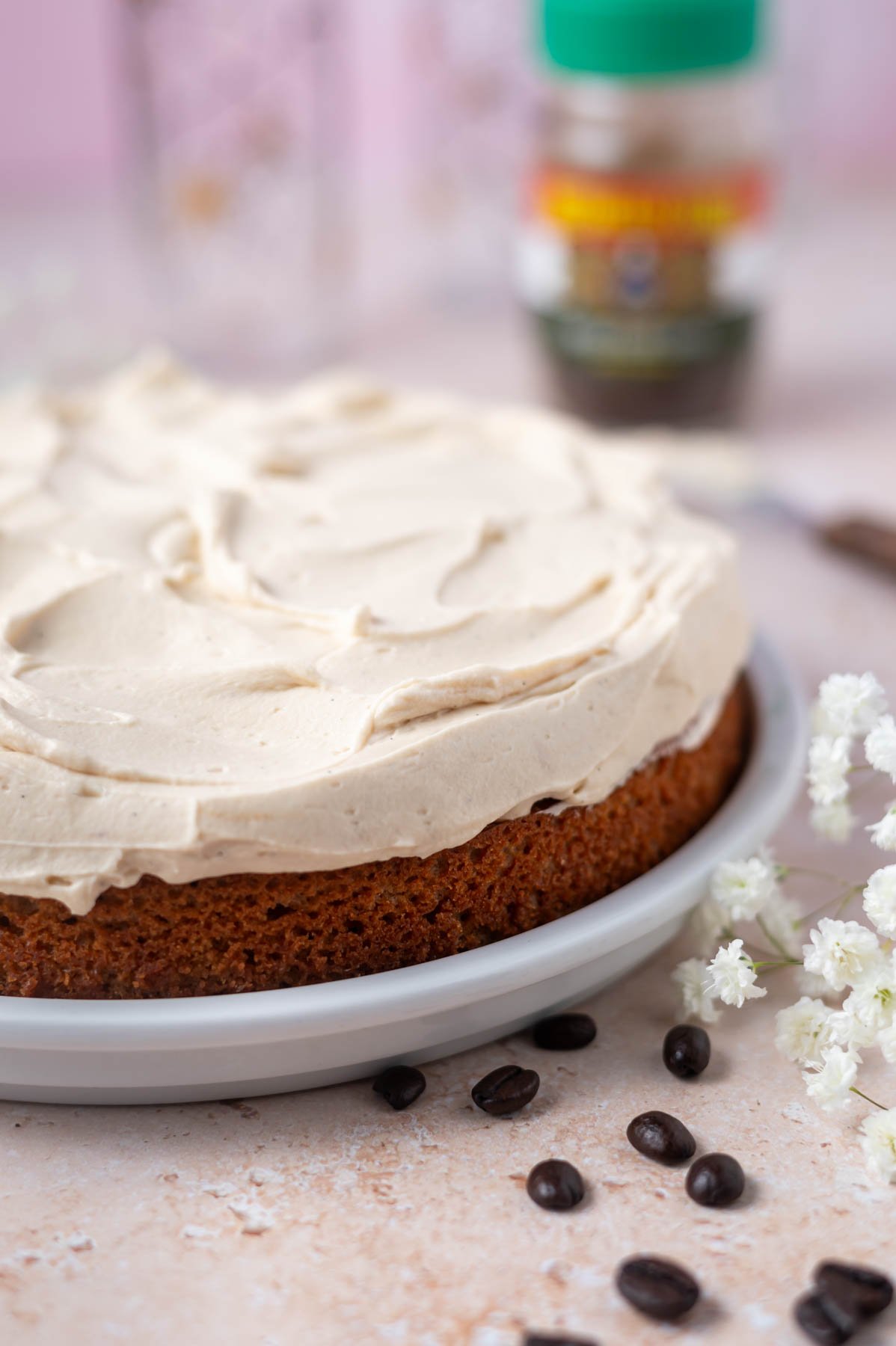 espresso cake on a cake plate with a layer of mascarpone frosting and coffee beans and fresh flowers in the foreground