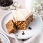 slice of cake on a plate with a bite on a fork with a glass of milk and a bowl of coffee beans in the background