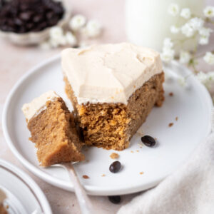 slice of cake on a plate with a bite on a fork with a glass of milk and a bowl of coffee beans in the background
