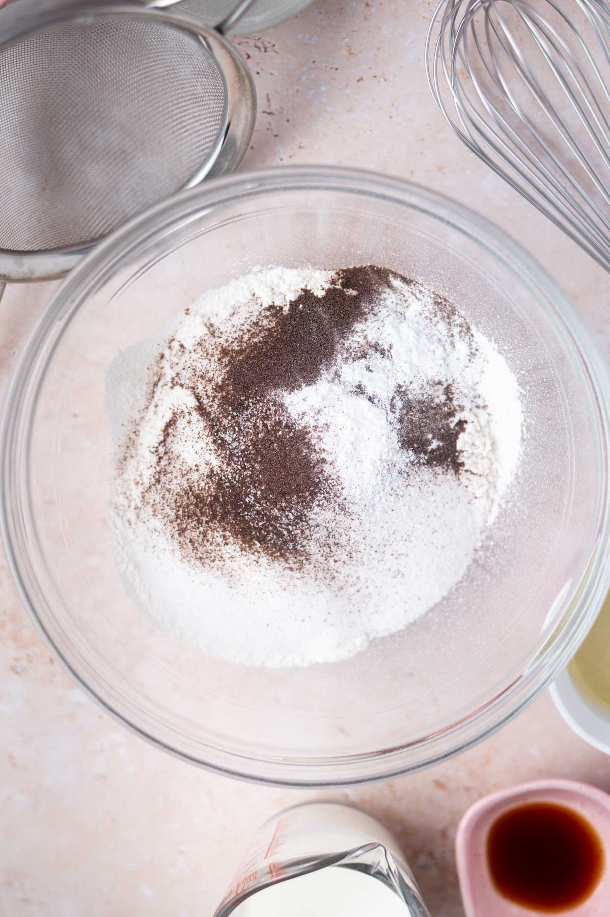flour, sugar, baking powder, salt and espresso powder in glass bowl with a whisk and sifter sitting nearby