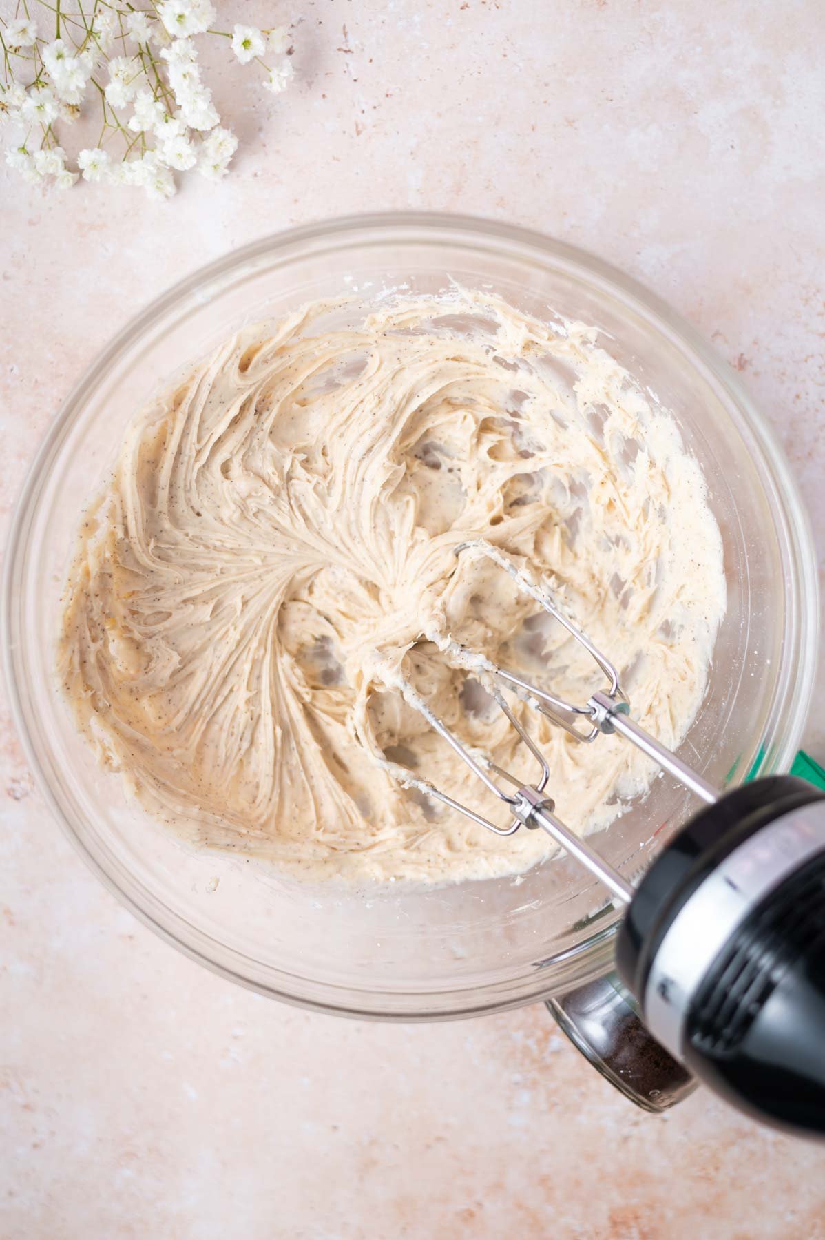 frosting ingredients beaten together in a glass bowl with a hand mixer