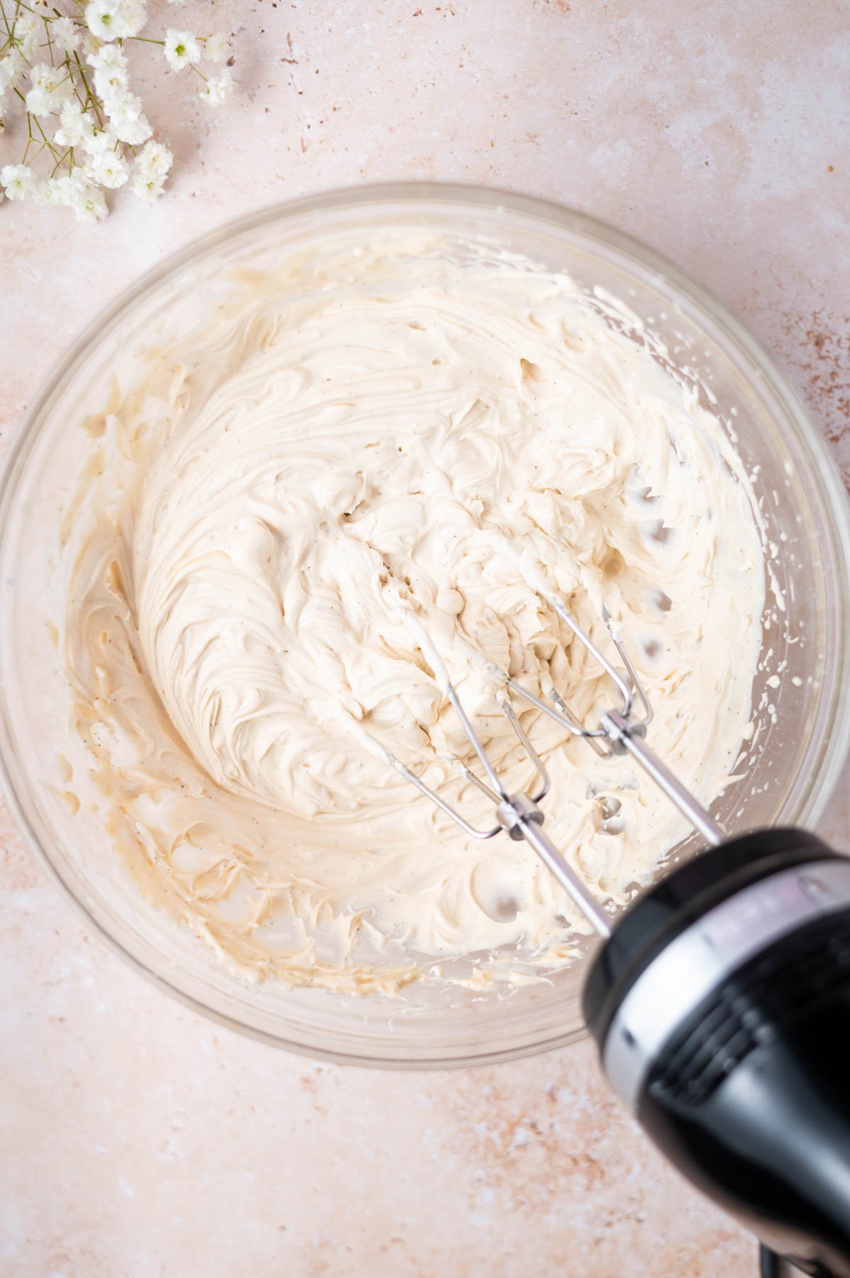 whipped espresso mascarpone frosting in a glass bowl with a hand mixer