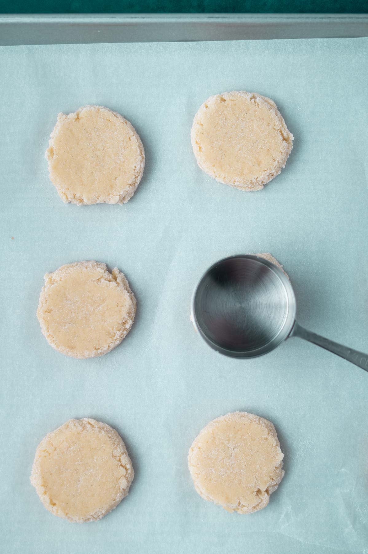 measuring cup flattening cookie dough balls on a parchment lined baking pan