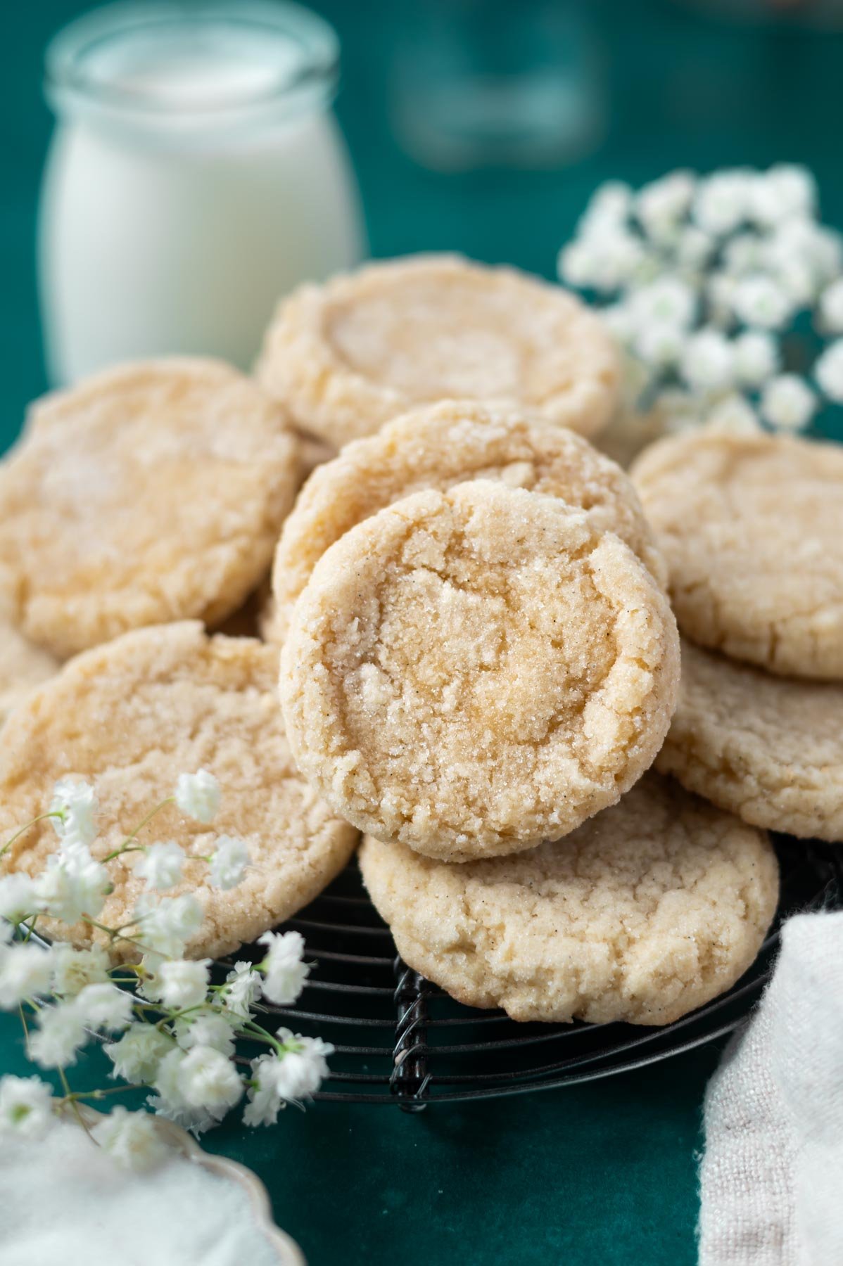 vanilla bean sugar cookies on a cooling rack with fresh flowers and milk in the background