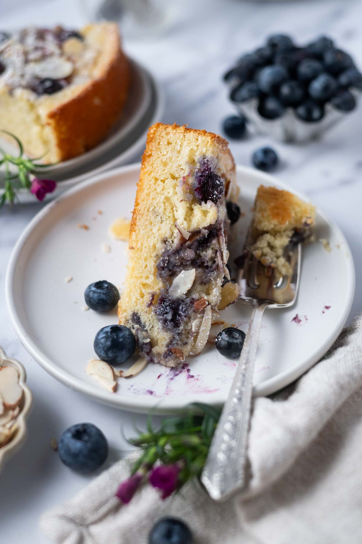 slice of cake on a plate with a fork and fresh blueberries in the background