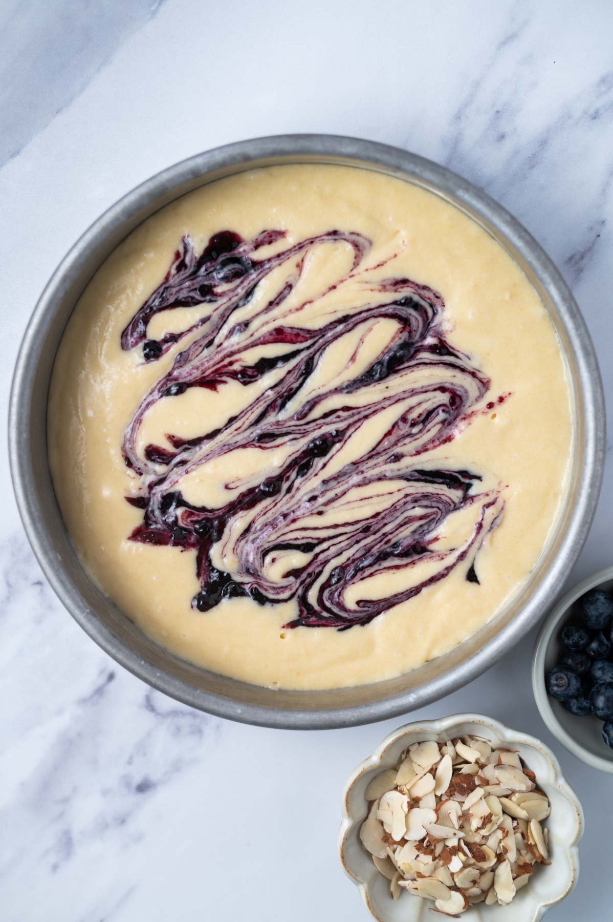 cake batter in a round cake pan with blueberry jam swirled into batter