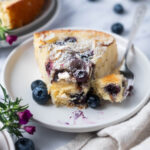 slice of blueberry almond cake on a plate with a bite on a fork and fresh blueberries