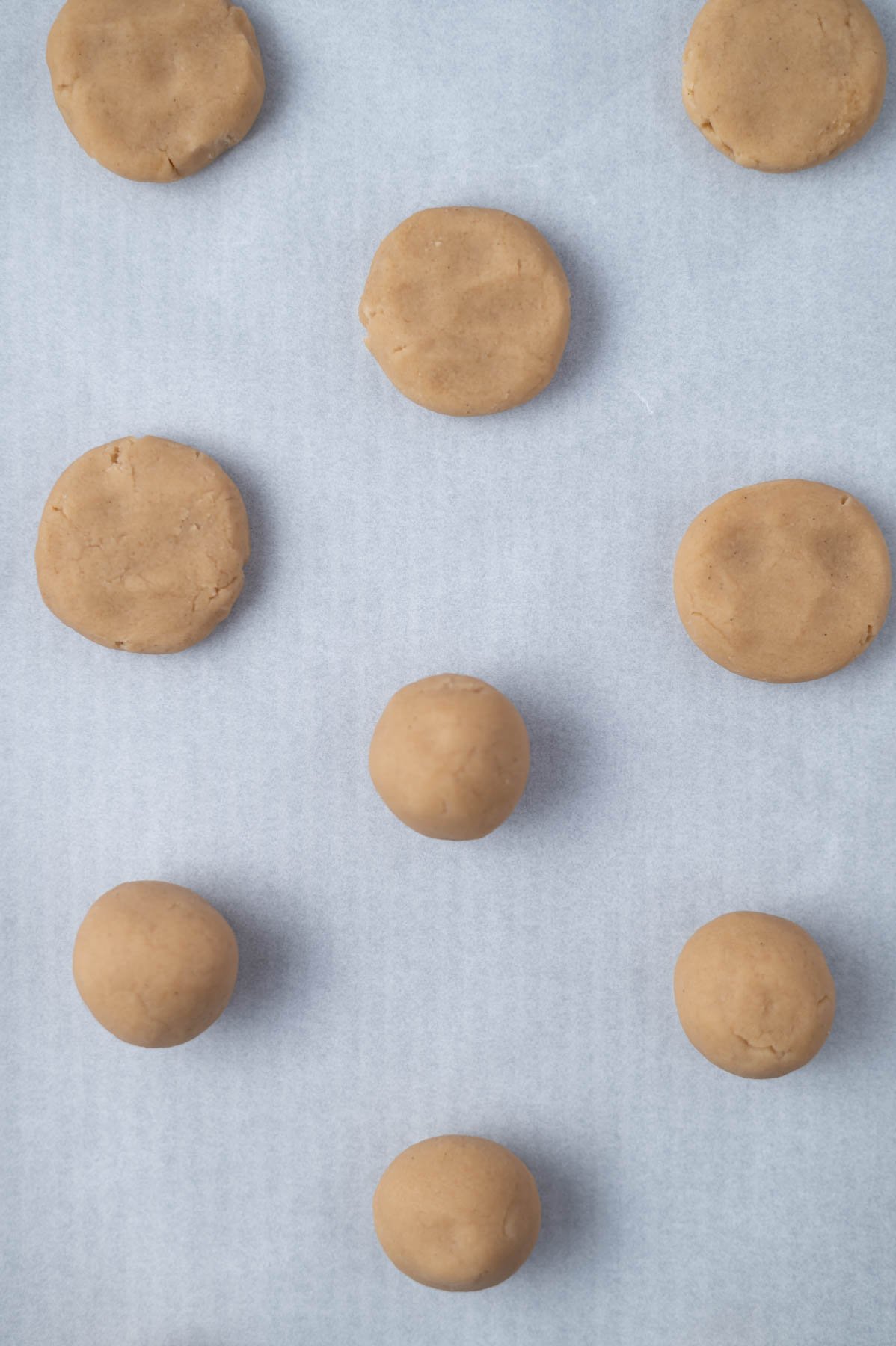 cookie dough balls and flattened cookie dough balls on a parchment lined baking sheet