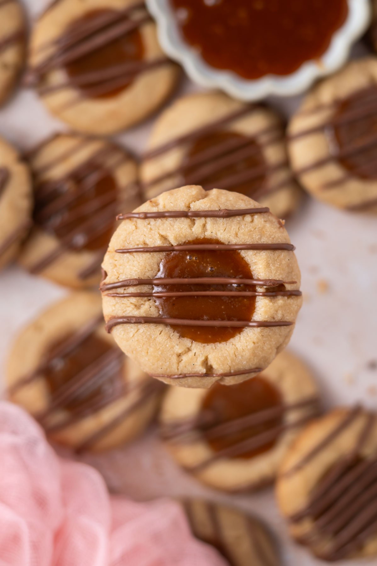 caramel thumbprint cookie appearing to be floating above other cookies and a bowl of caramel sauce