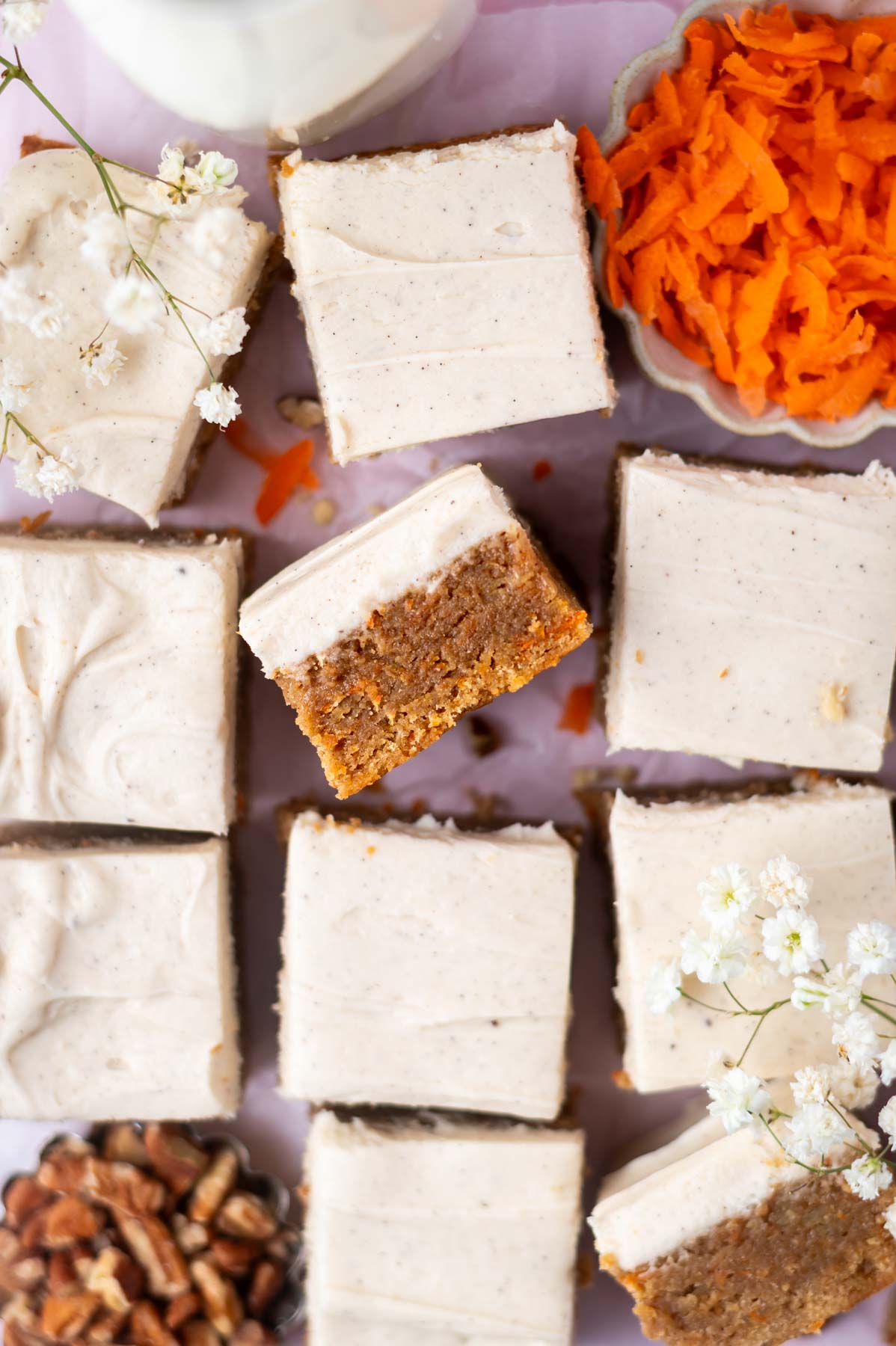 over head look at blondies with brown butter cream cheese frosting and a bowl of carrot shreds and pecan pieces