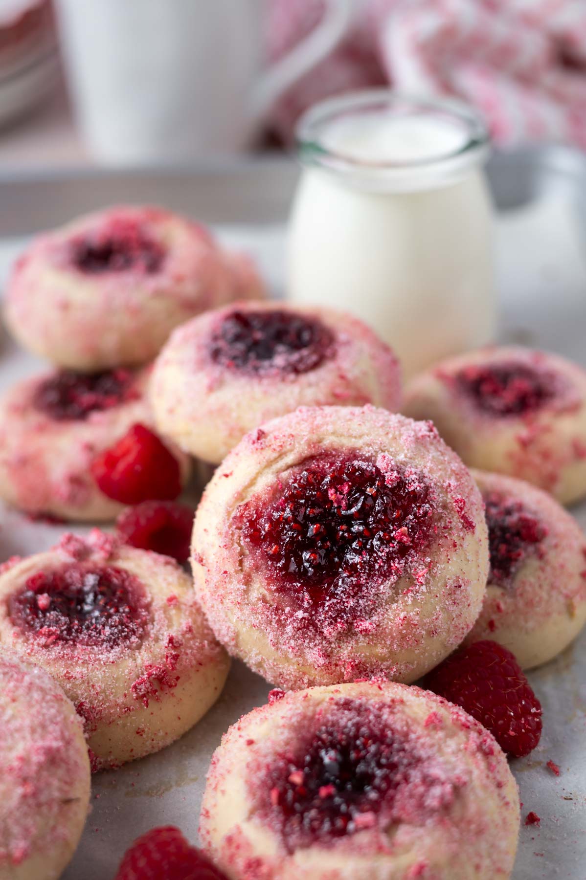 pile of raspberry donuts with fresh raspberries on parchment paper with a glass of milk and coffee