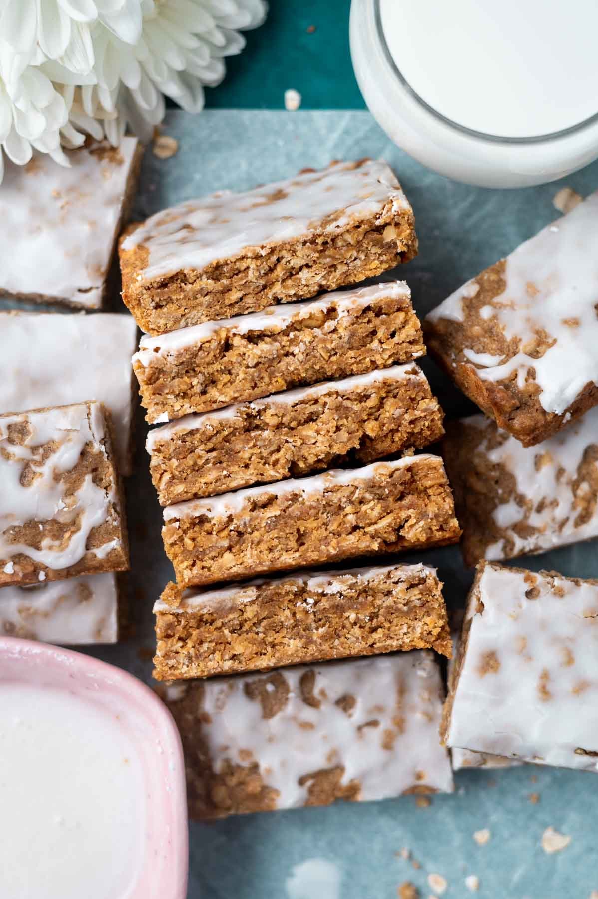 overhead look at iced oatmeal cookie bars on parchment paper with a glass of milk and extra icing