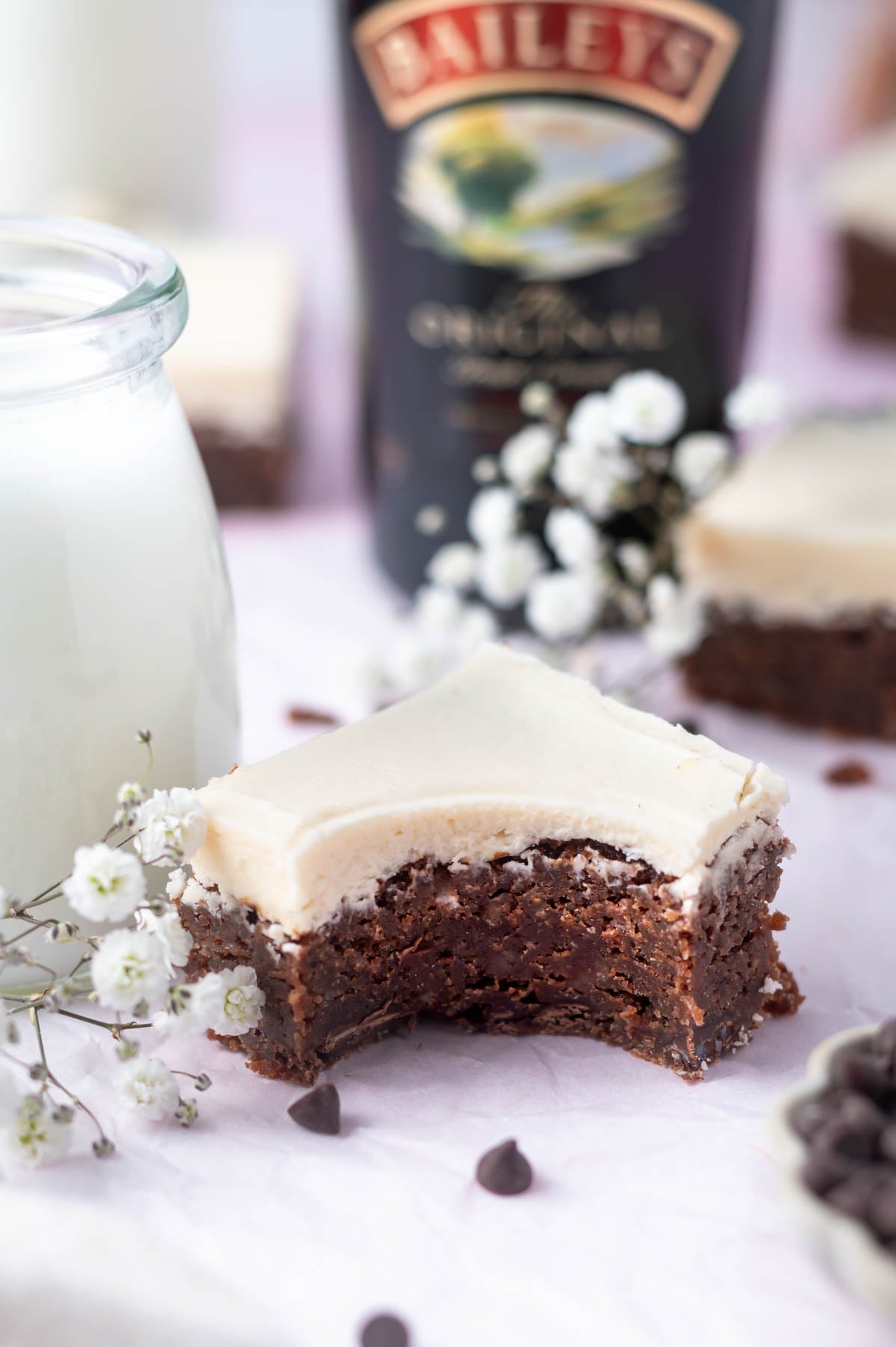 brownie with a bite missing next to a glass of milk with a bottle of Baileys in the background