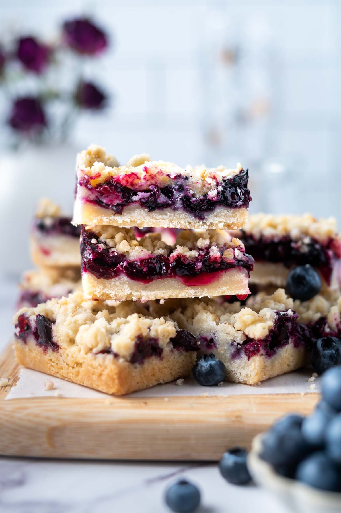 crumb bars stacked on a cutting board with flowers in the background