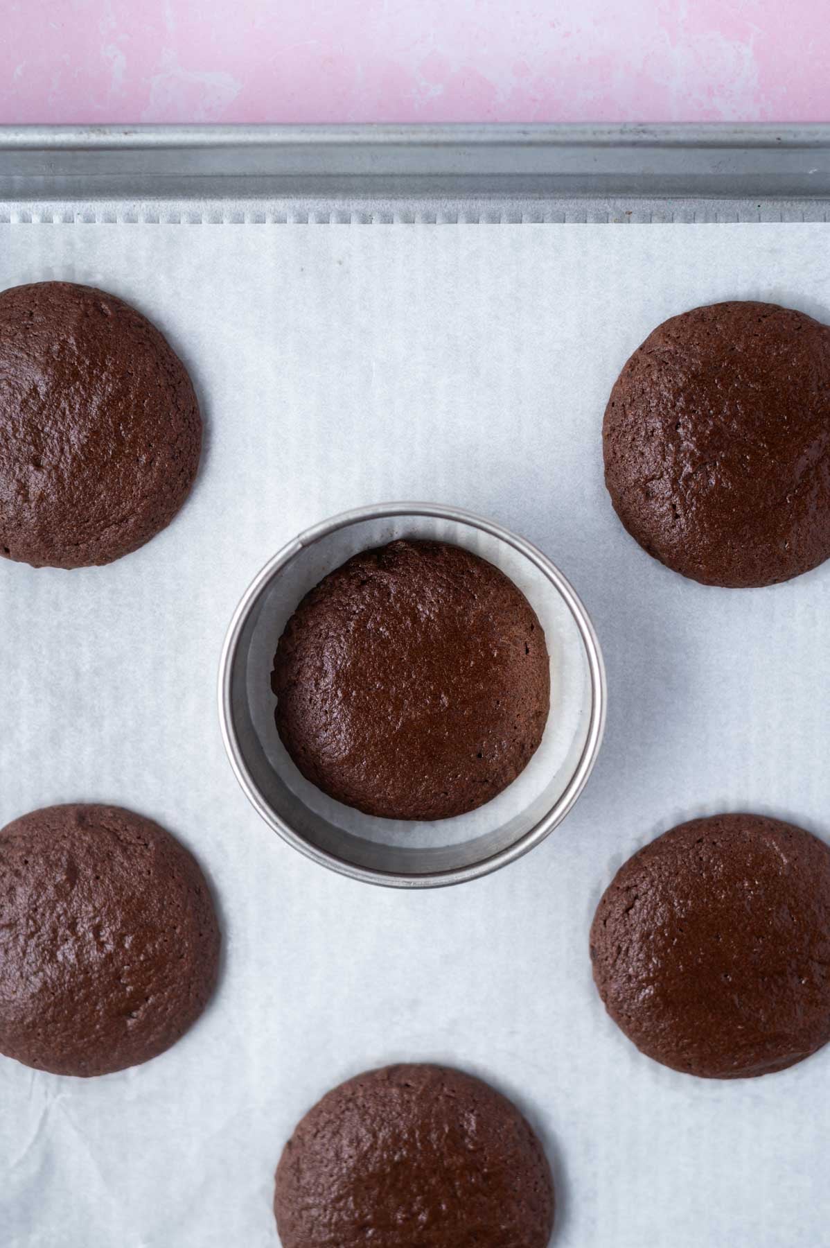 baked brownie cookies on a a baking pan with a biscuit cutter "scooting" a cookie