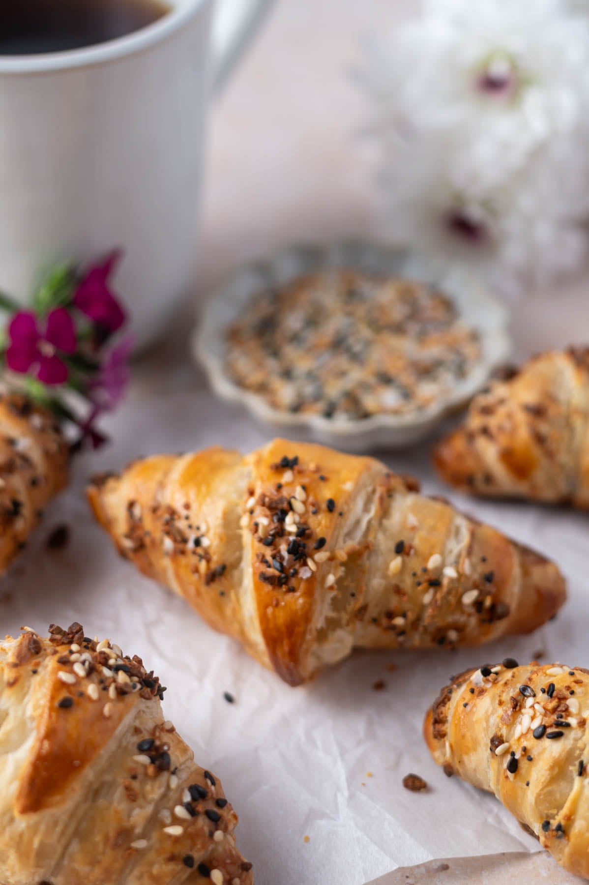 croissants on parchment paper with a bowl of everything seasoning an coffee in the background