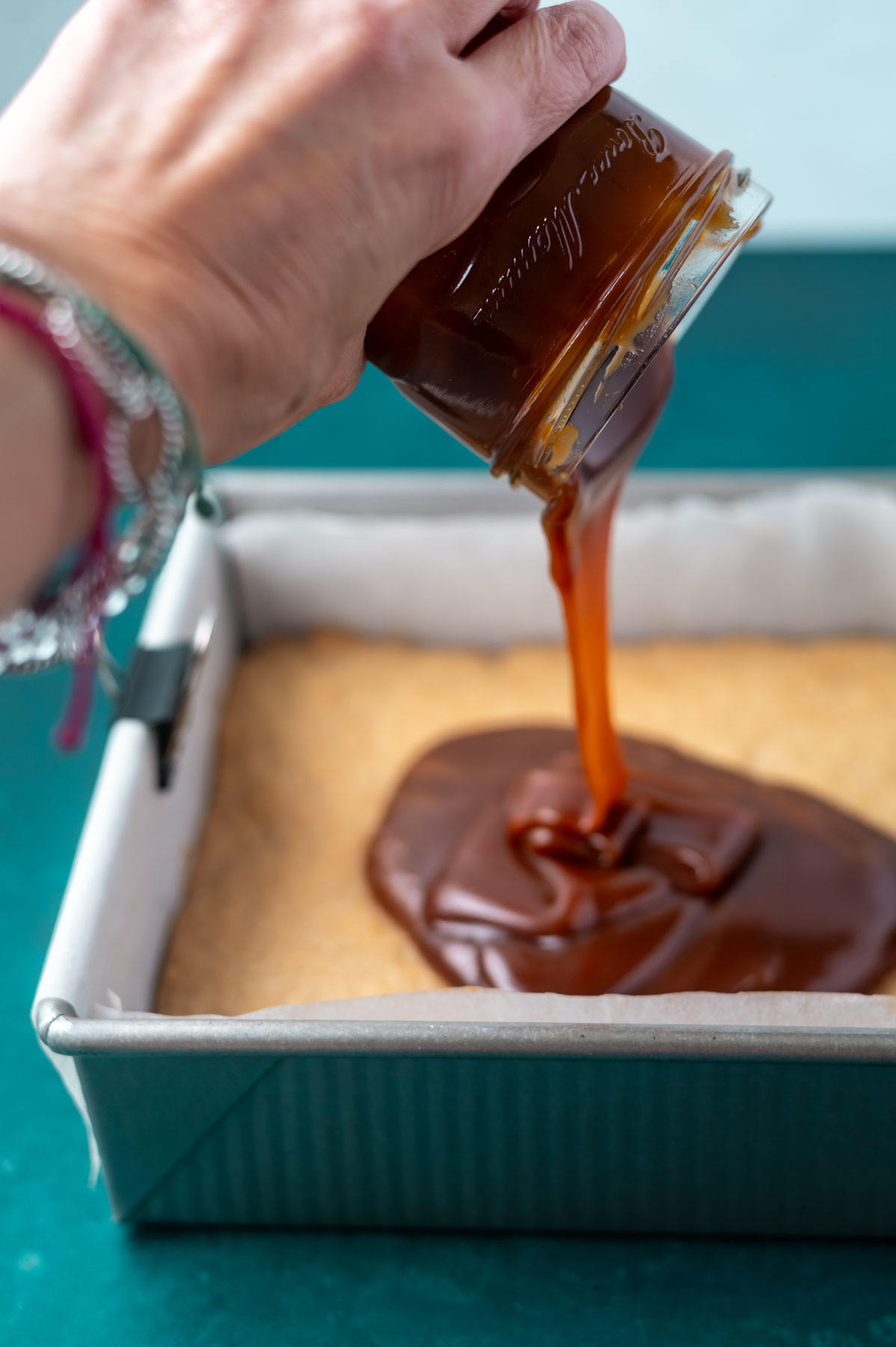hand pouring caramel sauce onto a biscuit base