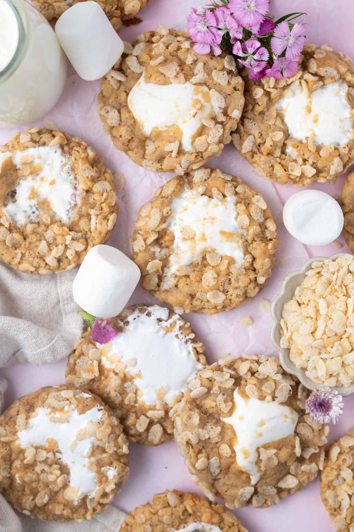 rice crispy cookies on a pink background with large marshmallows, flowers and a glass of milk