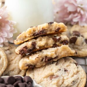 stack of broken chocolate chip cookies without brown sugar with a glass of milk and pink flowers