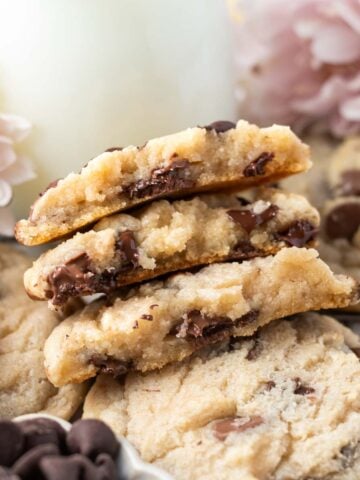 stack of broken chocolate chip cookies without brown sugar with a glass of milk and pink flowers
