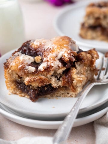 slice of cinnamon focaccia on a plate with a fork with a glass of milk in the background