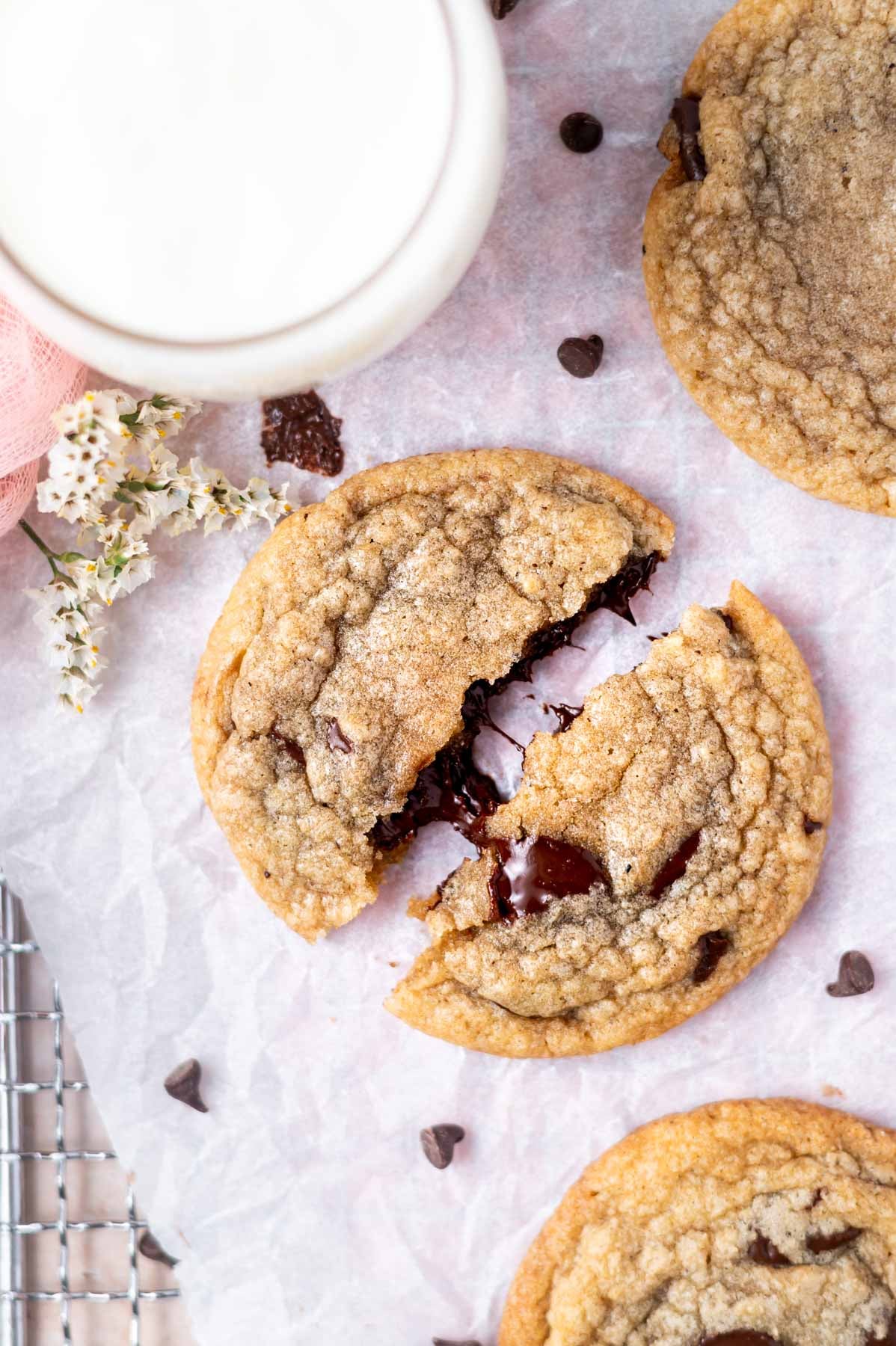 broken cookie on a parchment lined cooling rack with a glass of milk
