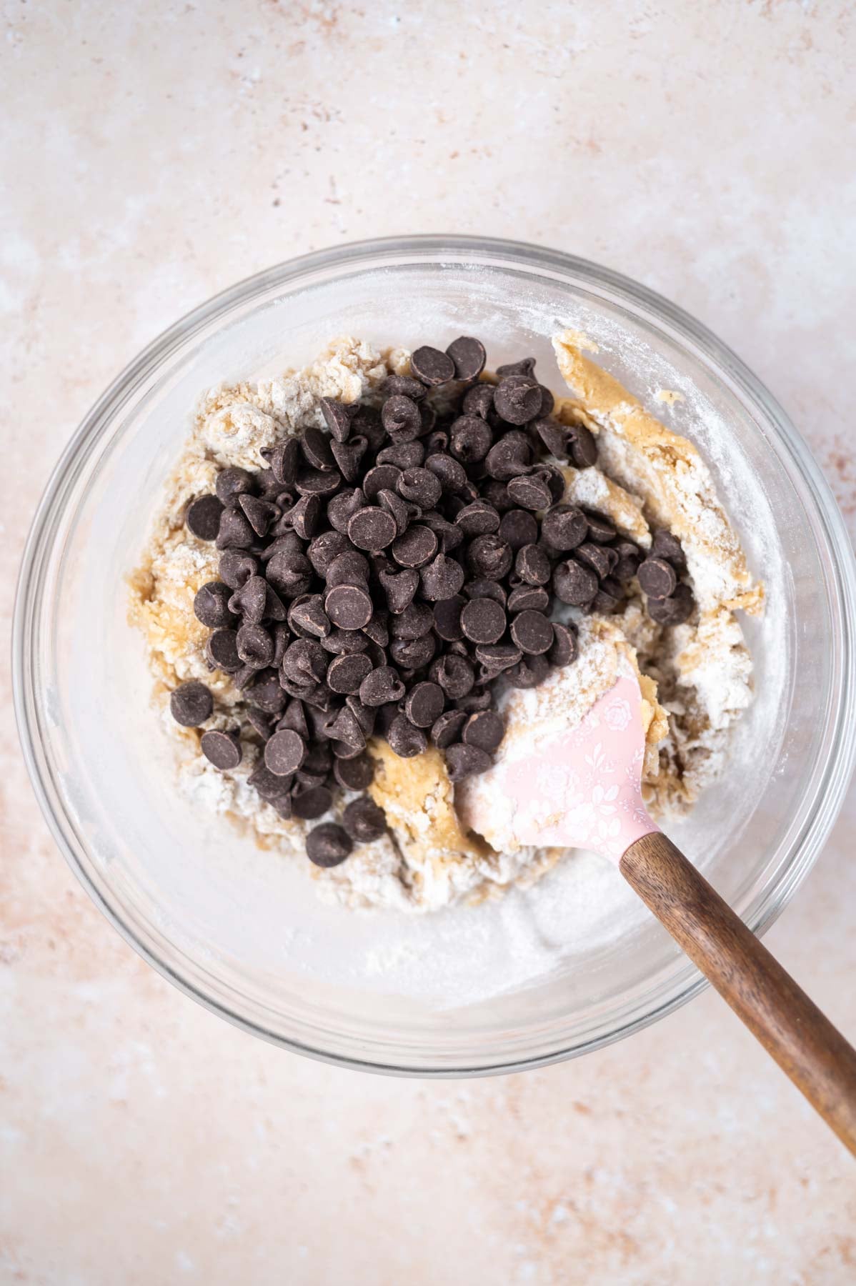 chocolate chips added to cookie dough in a bowl with a bit of flour still showing in the dough