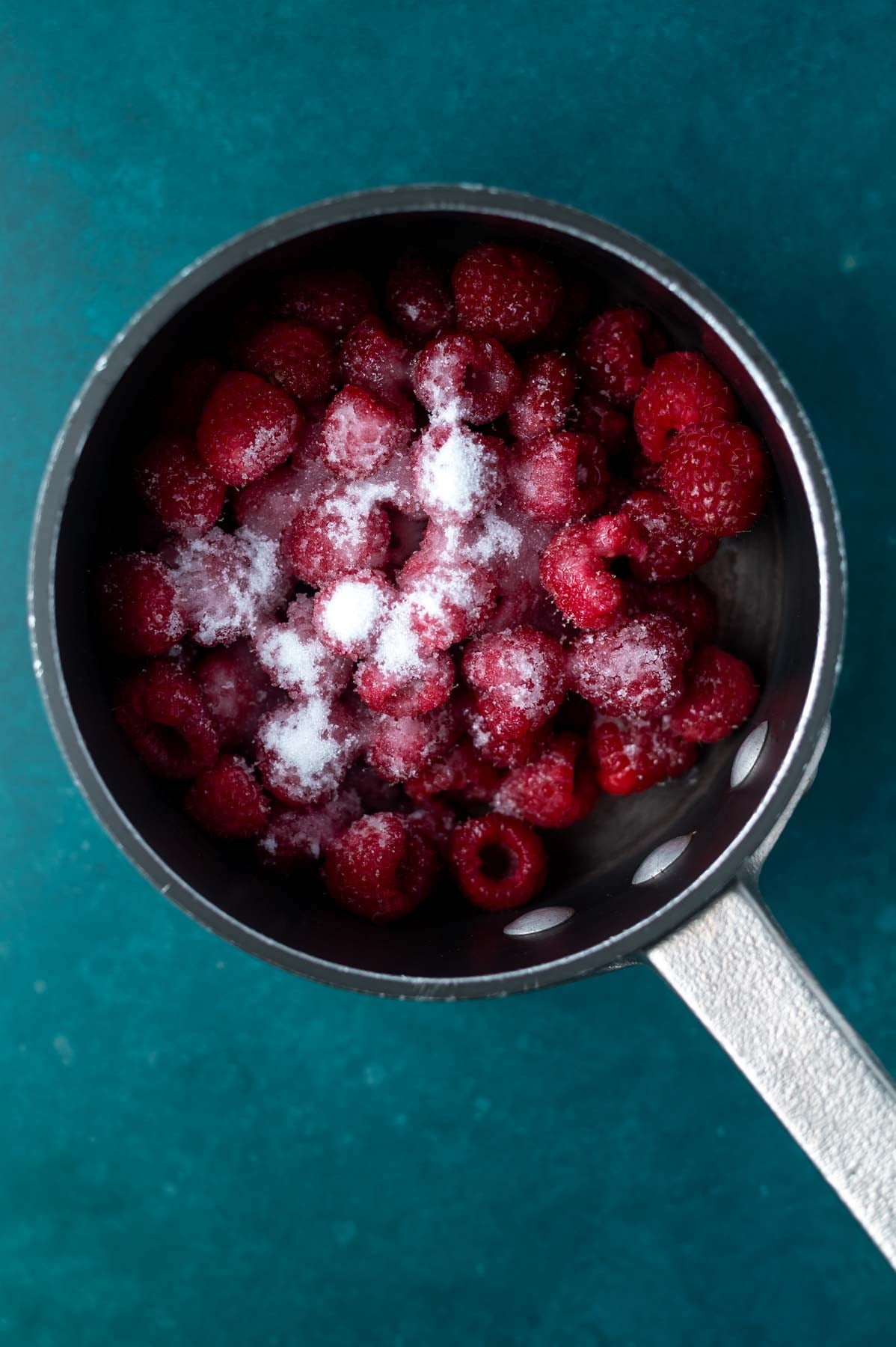 sugar sprinkled over raspberries in a saucepan