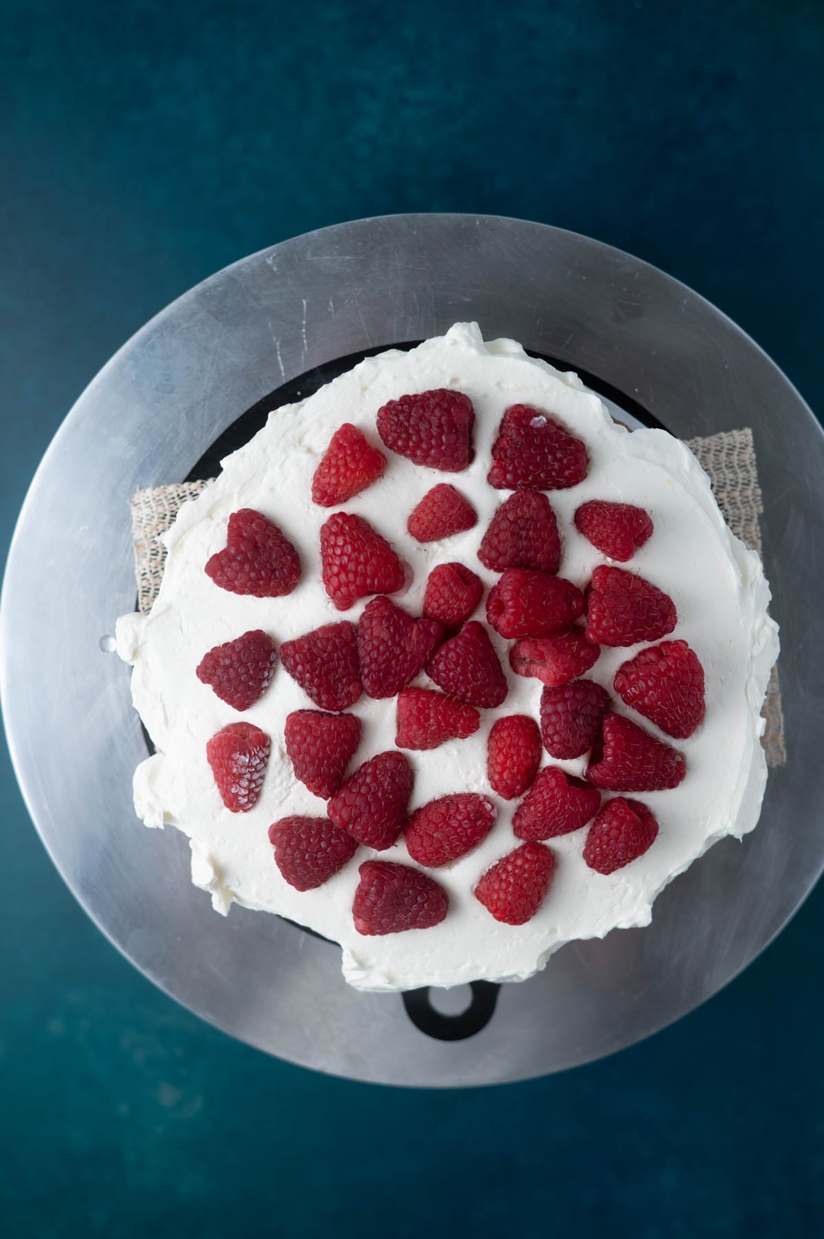 fresh raspberries on buttercream covered cake layer on top of a cake turntable