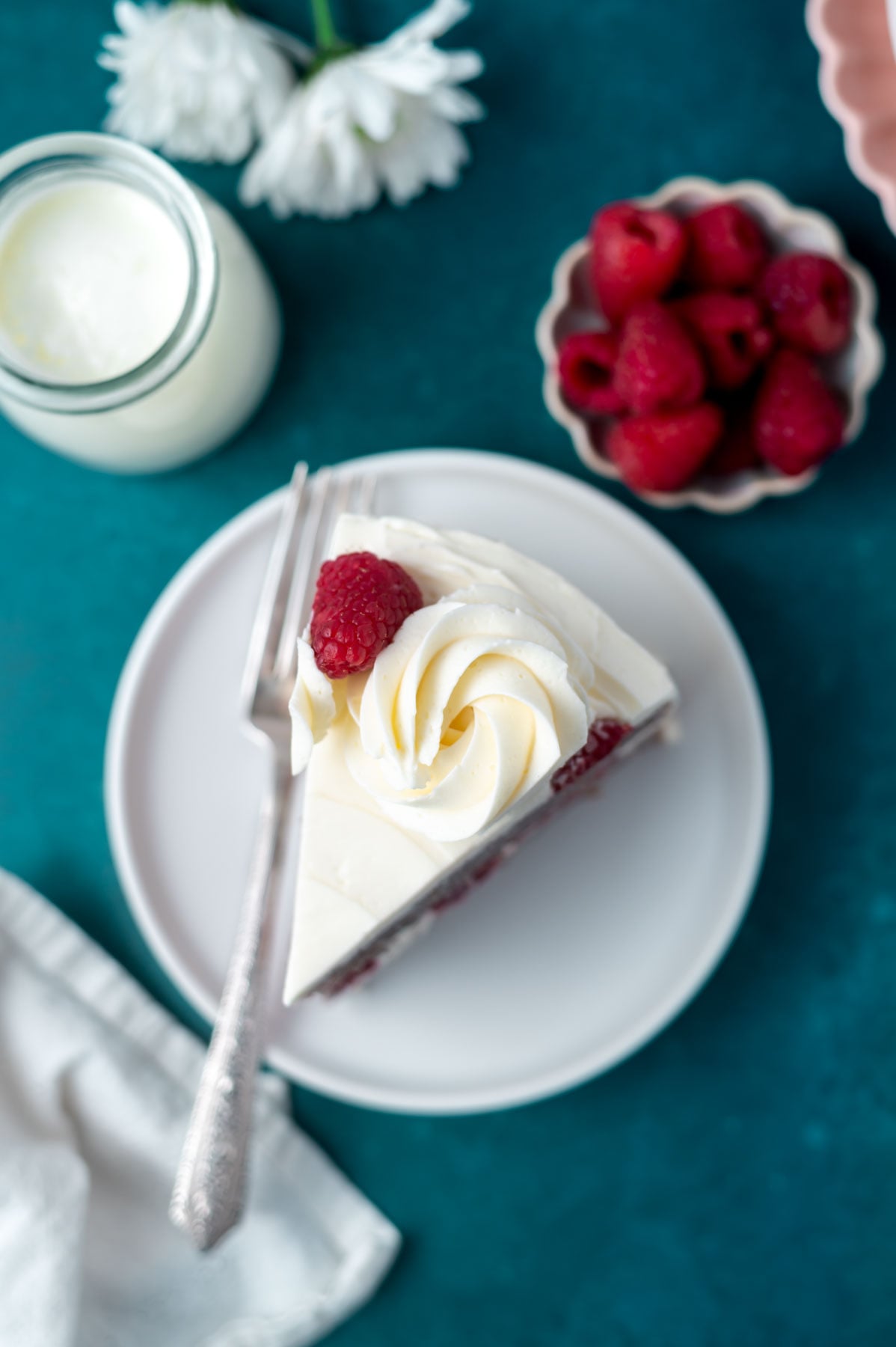overhead look at a slice of cake on a plate with a fork and a glass of milk and bowl of berries