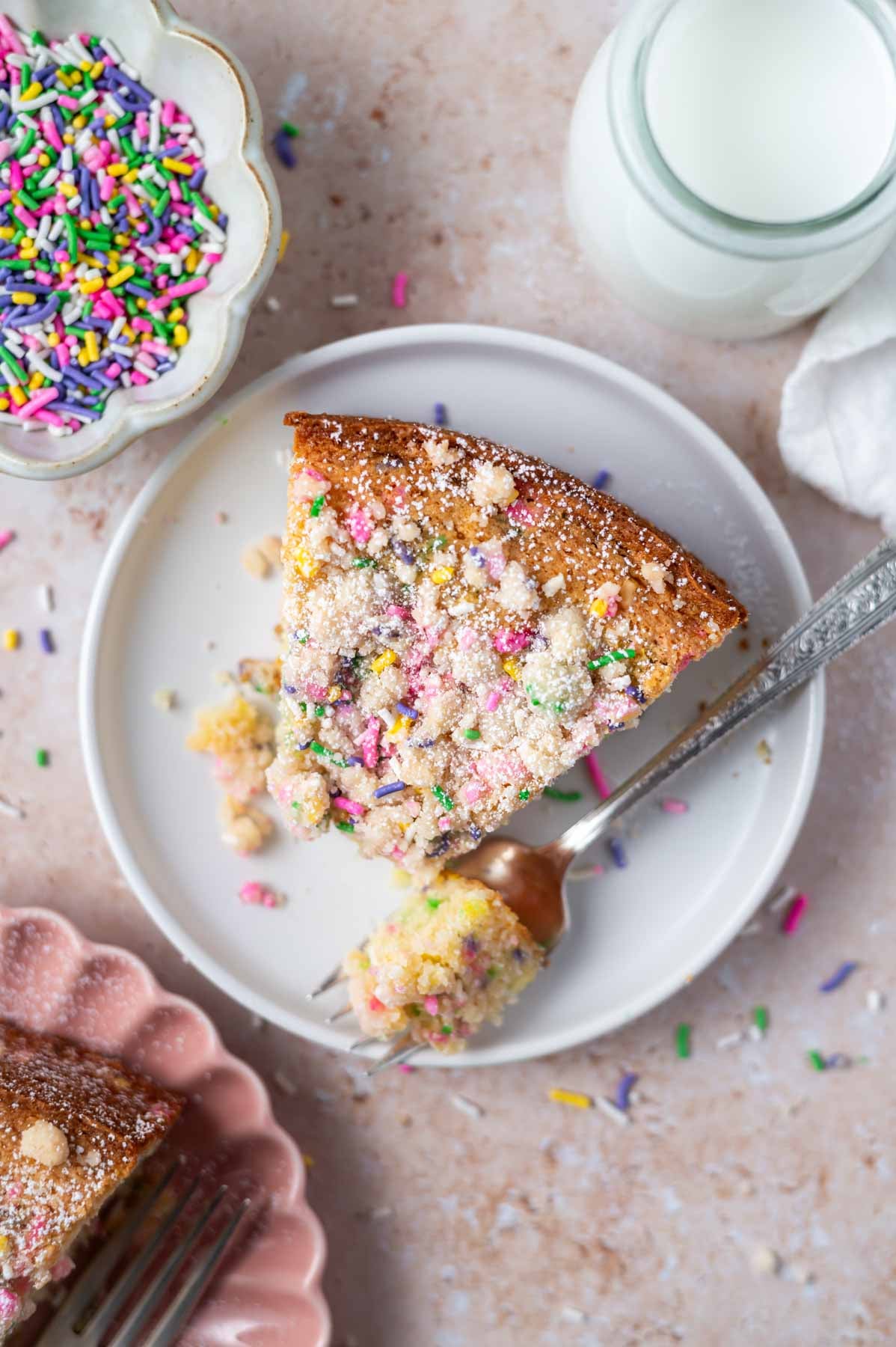 slice of sprinkle cake on a plate with a bite on a fork and a glass of milk