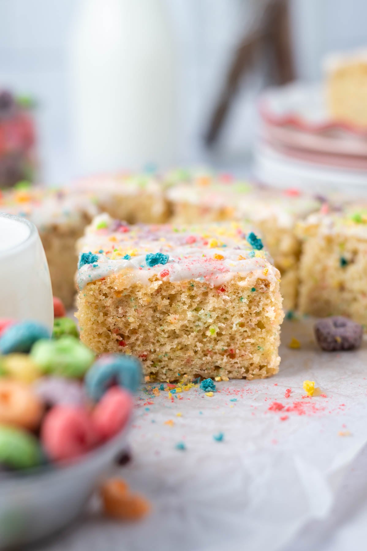 slice of cereal cake on parchment paper with a bowl of Froot Loops in the foreground