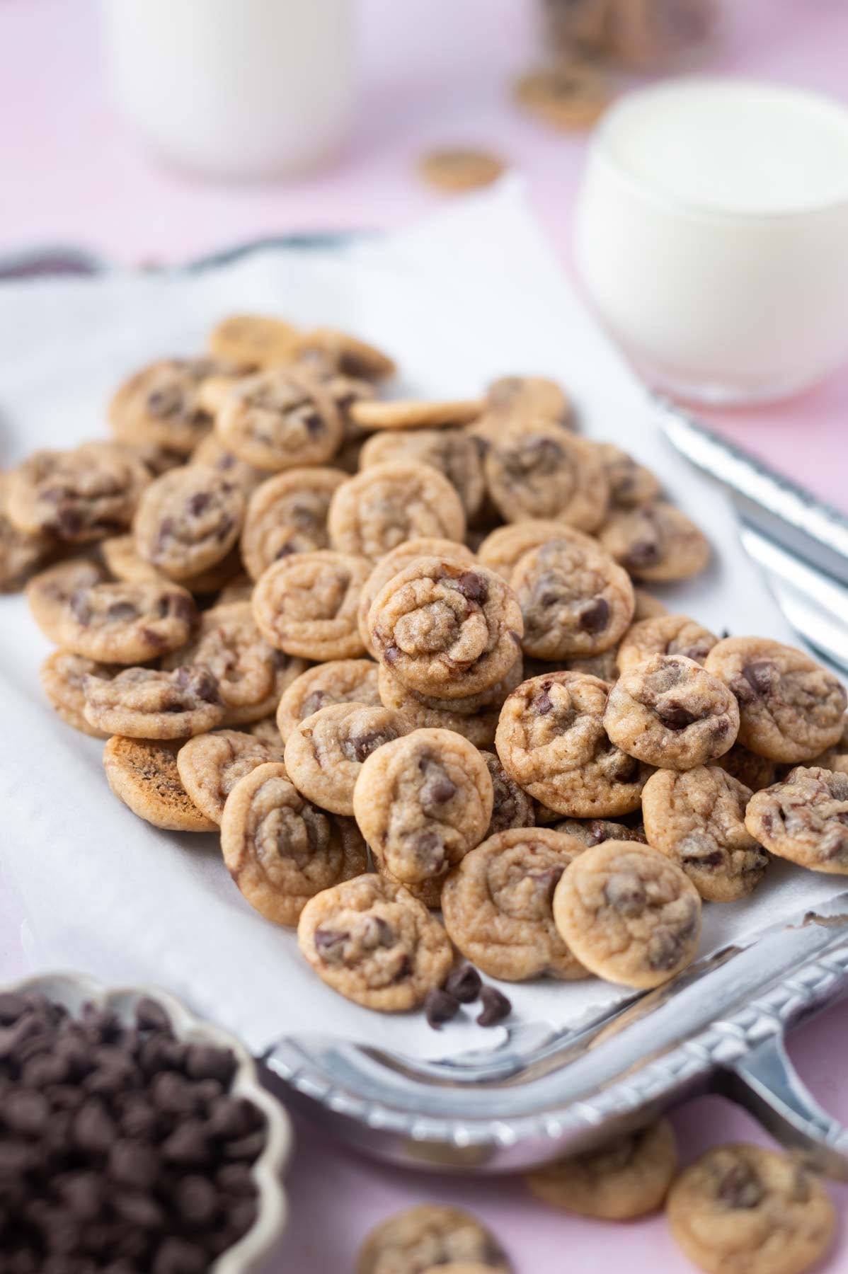 pile of mini chocolate chip cookies on a tray with milk in the background
