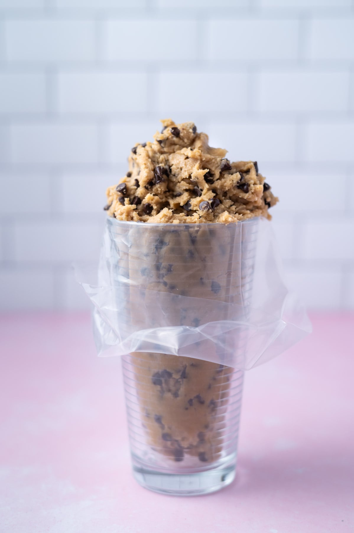 tall glass lined with a piping bag and filled with chocolate chip cookie dough