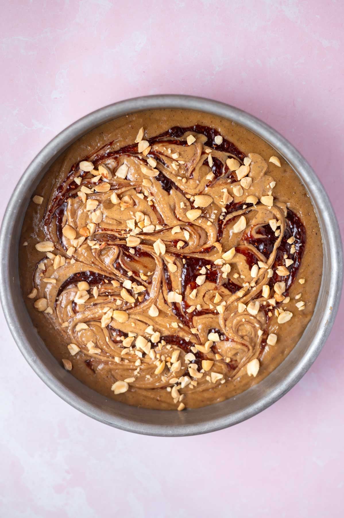 peanut butter and jelly swirl with peanuts over cake batter in a baking pan