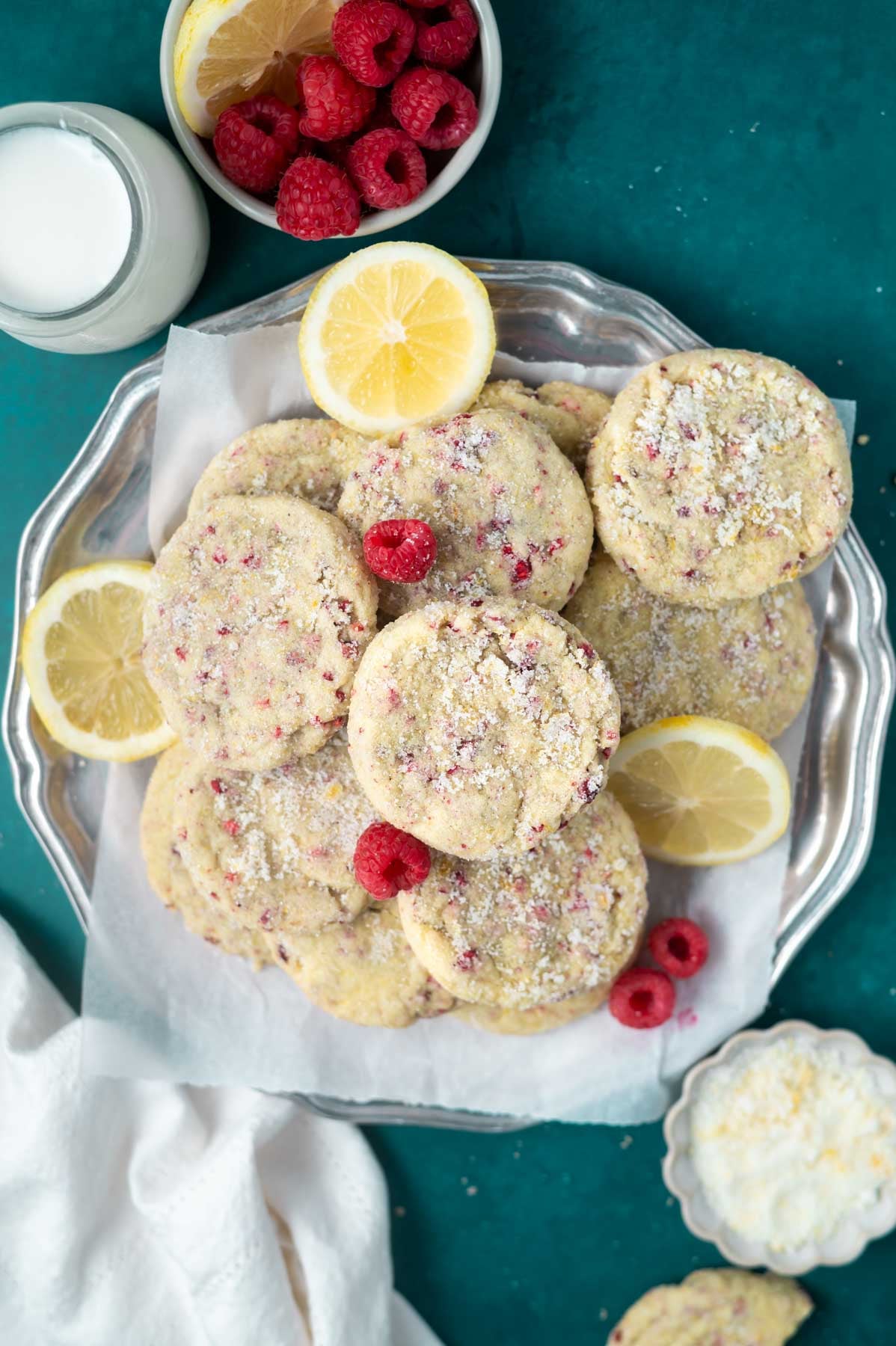 plate of cookies with a glass of milk and a bowl of raspberries and lemon slices