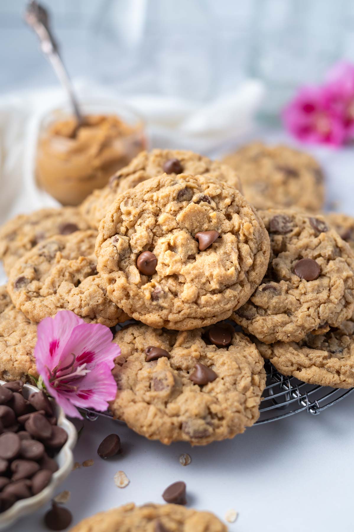 pile of cookies on a cooling rack with a bowl of peanut butter and chocolate chips nearby