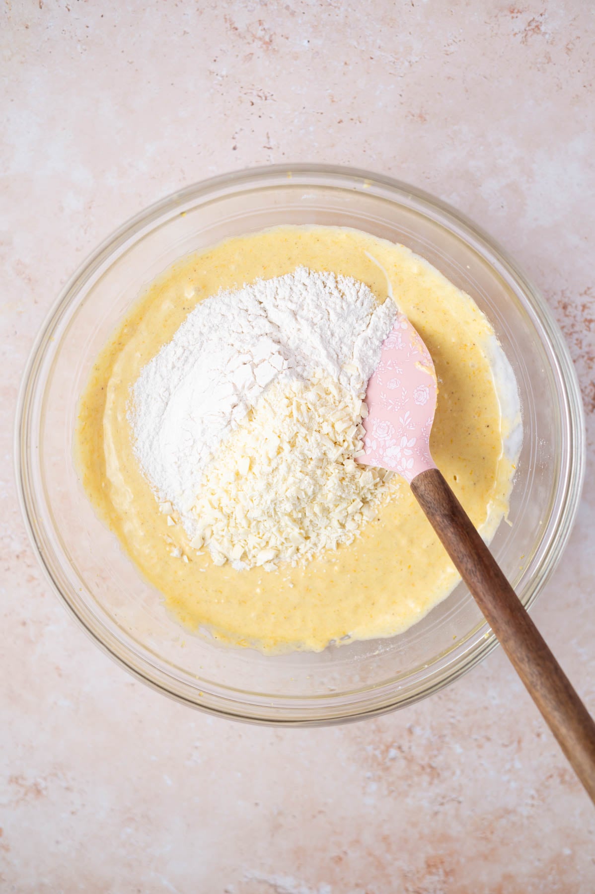flour and white chocolate being mixed into cake batter with a spatula